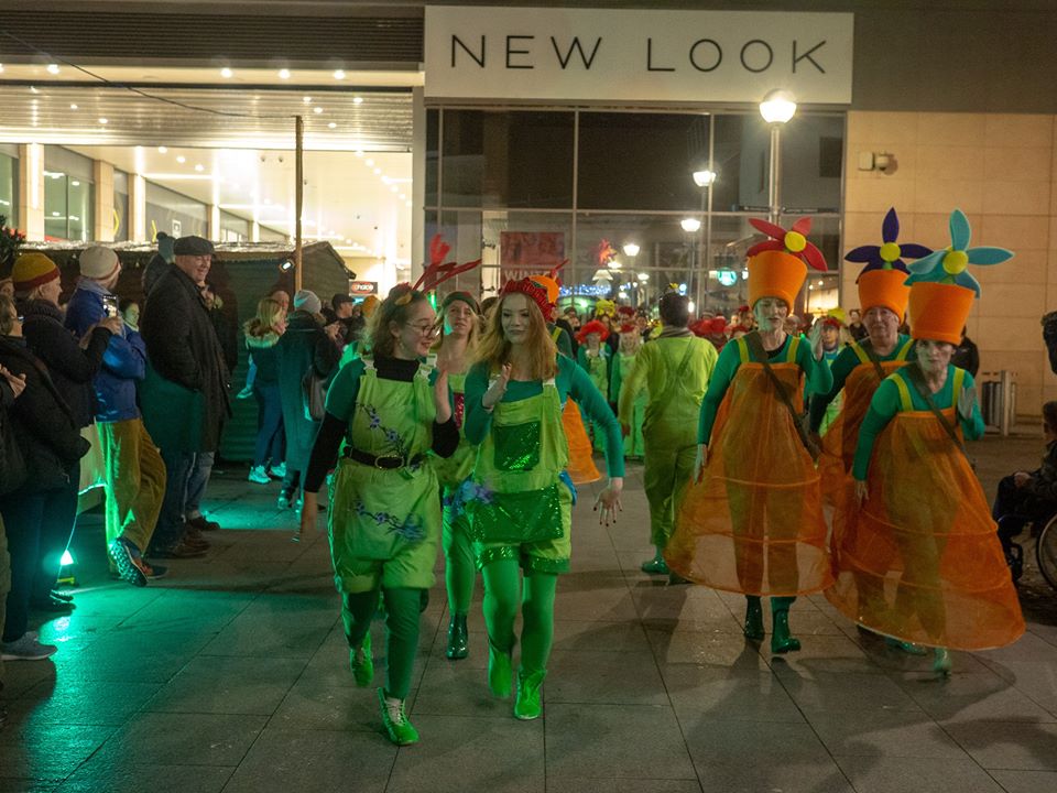 Young dancers in green and older in orange costume in shopping centre