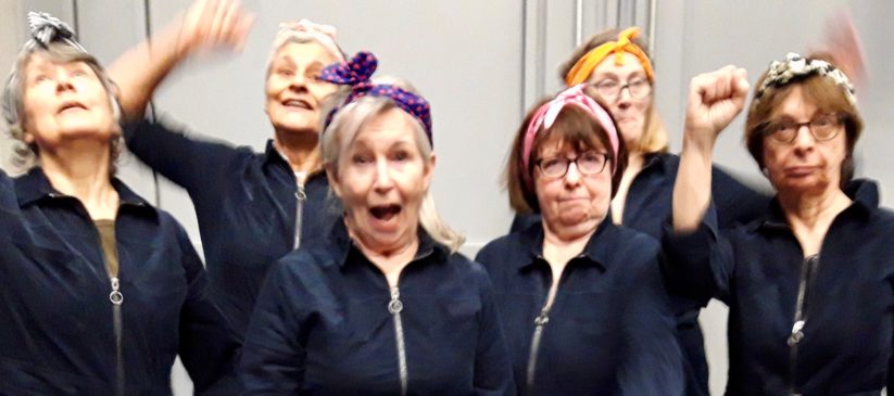 Faces of 6 women posing in blue boiler suits and headscaves