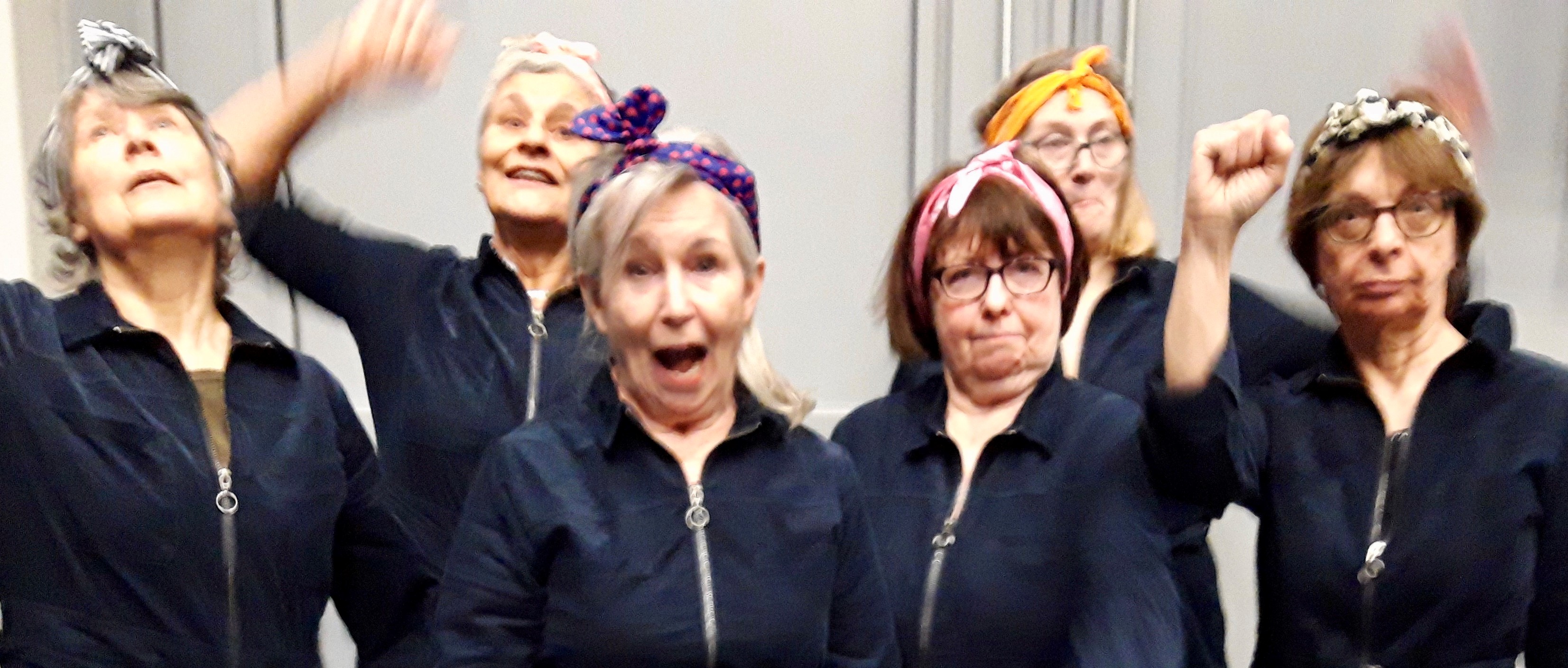 Faces of 6 women posing in blue boiler suits and headscaves