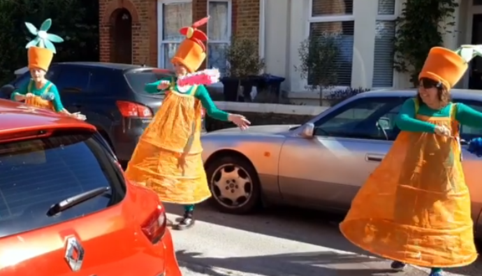 Three dancers dressed as flowerpots dance in a road