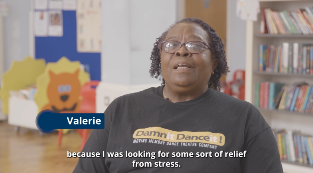 Video testimonial of Valerie wearing a Moving Memory t-shirt, speaking in a room with bookshelves. A graphic names her "Valerie" alongside subtitles about finding stress relief.