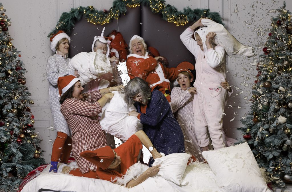7 women dressed in Christmas pyjamas have a pillow fight
