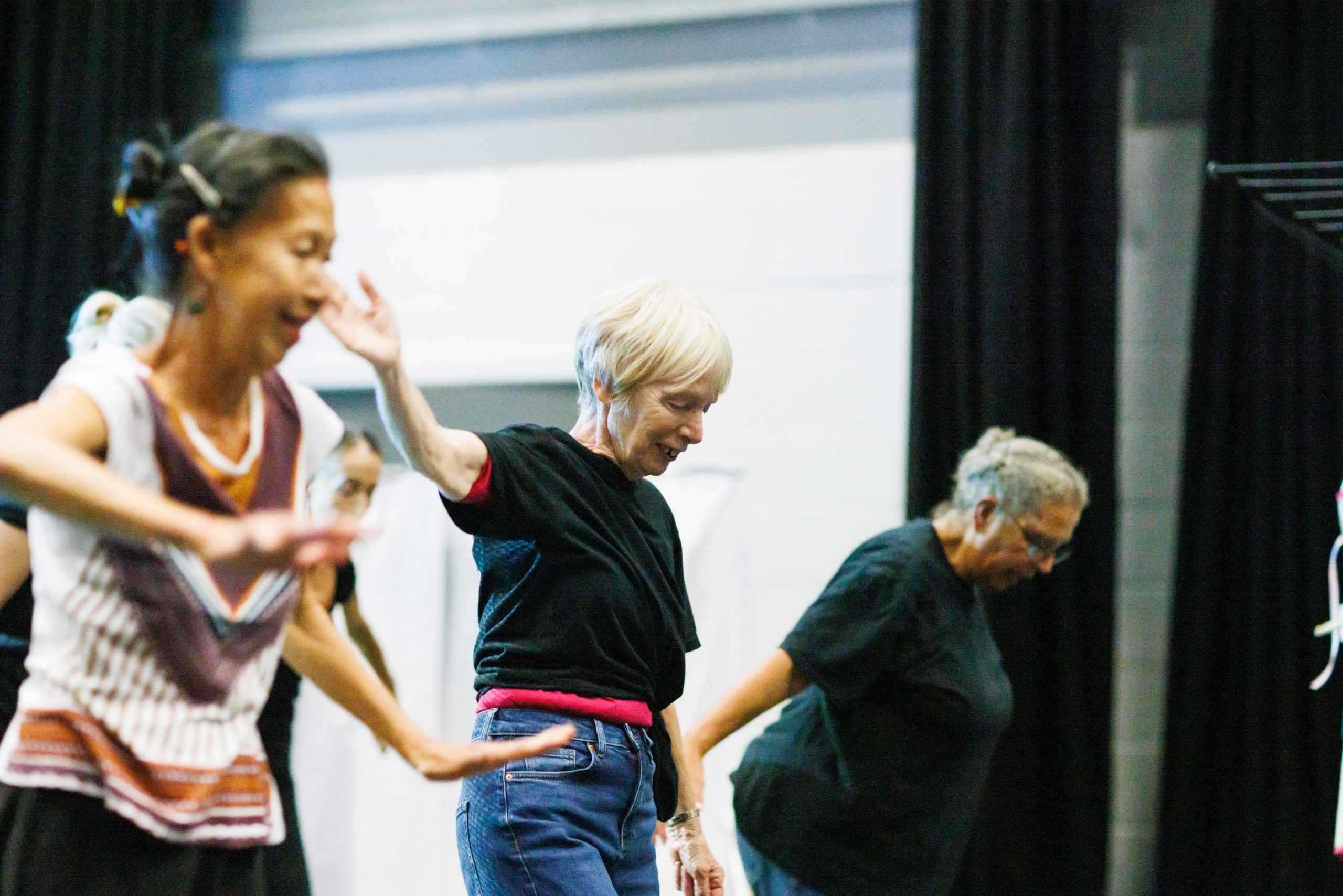 3 women stand in a line dancing with the arms stretched out.