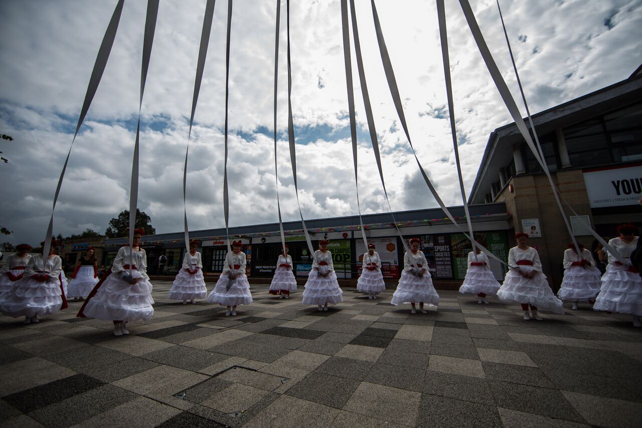 Women in white dresses hold on to giant maypole ribbons.