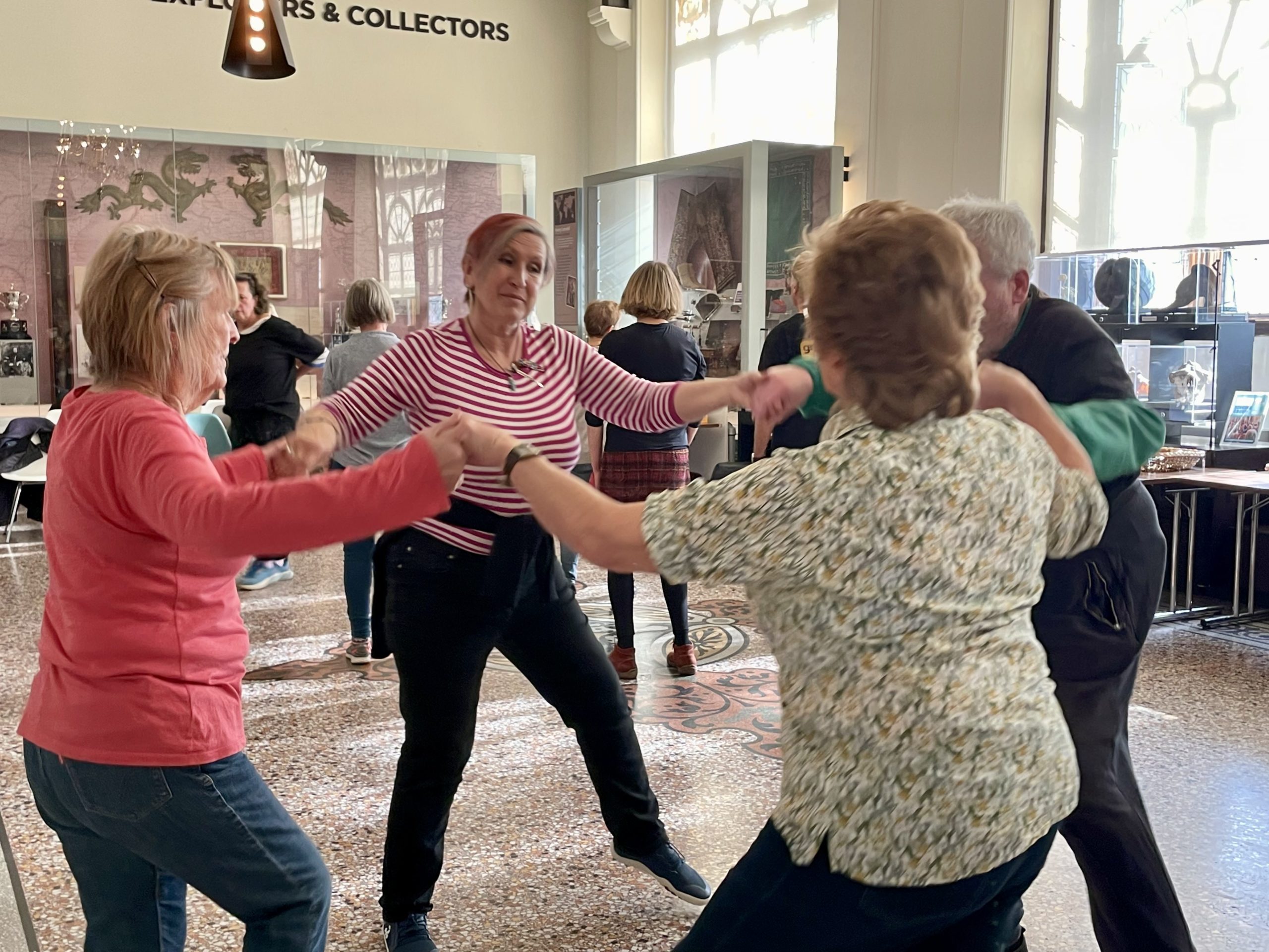 Four performers hold hands in a circle mid-movement. They wear an array of different colours and patterns.