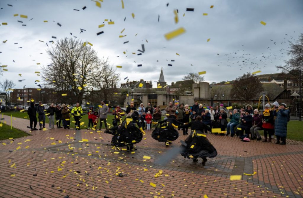 Moving Memory perform Cracking the Crinoline at Dover Winter Light Up in Pencester Gardens, Dover. Yellow confetti flies around.