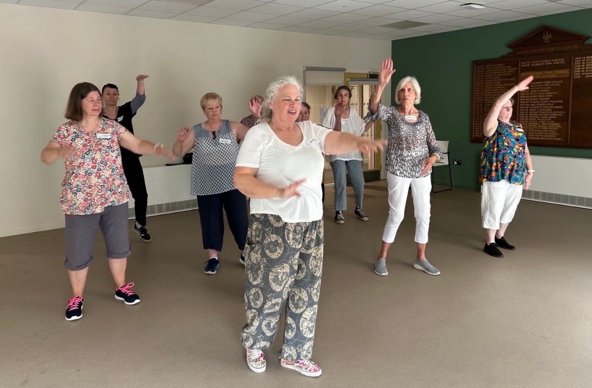 A group of older women dance and hold up their arms during a movement workshop.